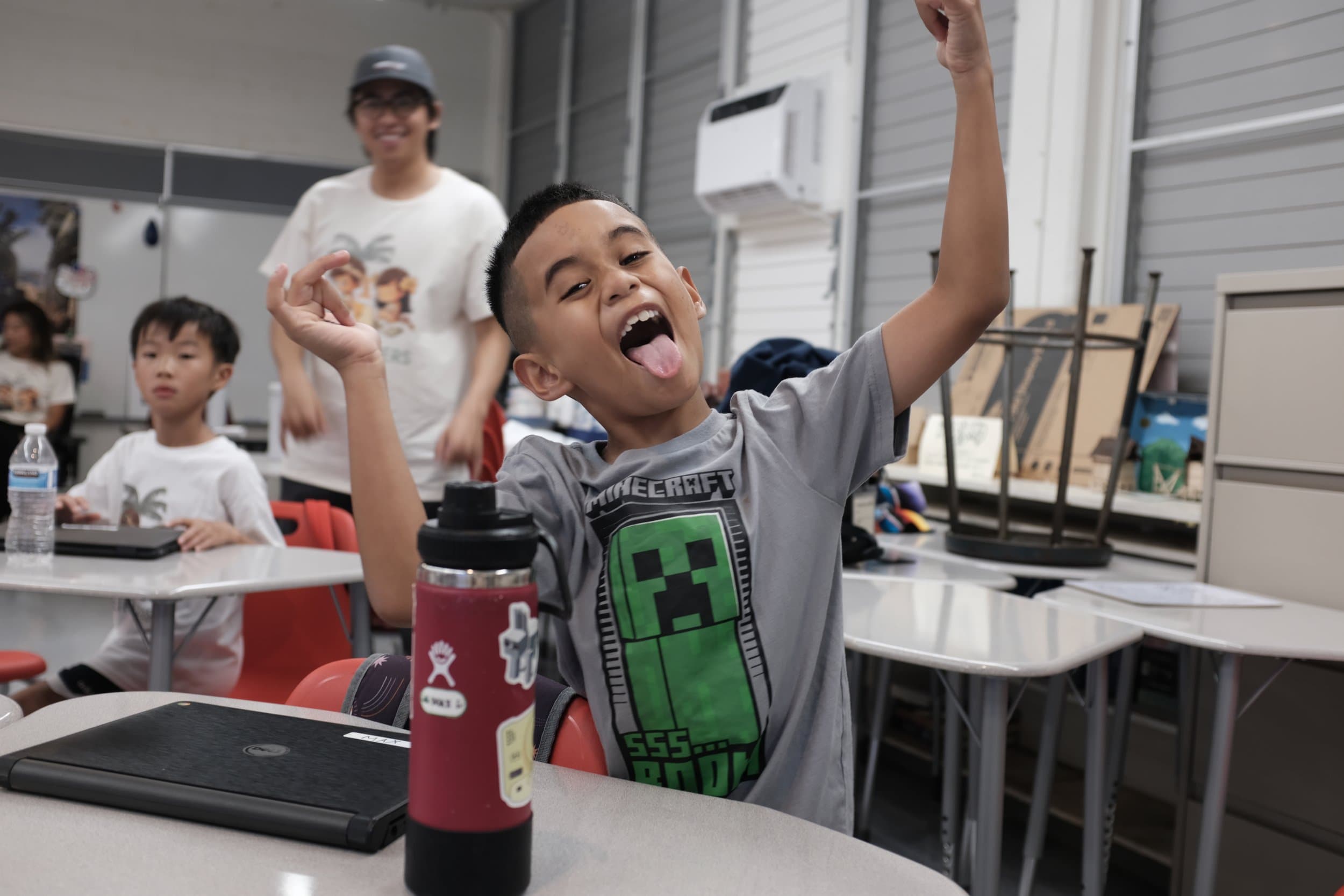 A boy in a grey Minecraft t-shirt making a playful gesture with his tongue sticking out.